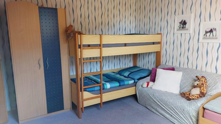 Een gezellige kinderkamer met een stapelbed en een bank. De muren zijn versierd met kleurrijke patronen, en er zijn een paar afbeeldingen van dieren.