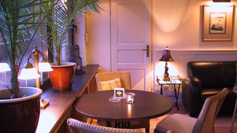 Ein gemütlicher Wohnbereich mit einem runden Tisch und bequemen Stühlen. Sanftes Licht und Pflanzen schaffen eine entspannte Atmosphäre.