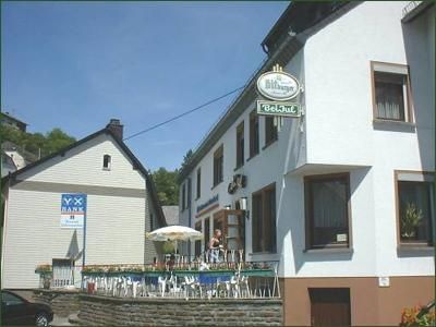 Ein gemütliches Gasthaus mit Tischen und Stühlen auf der Terrasse. Im Hintergrund sind grüne Hügel sichtbar.