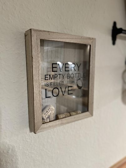 Un cadre décoratif avec l'inscription «Chaque bouteille vide est remplie d'amour». À l'intérieur, quelques bouchons sont visibles.