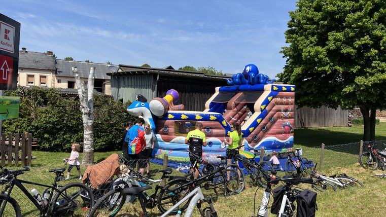 Ein bunter Hüpfburg steht in einem grünen Garten, umgeben von Fahrrädern. Kinder haben Spaß beim Spielen.