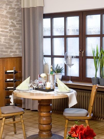 Een gezellig tafeltje met witte wijn en glazen in een warme kamer. Grote ramen laten veel licht binnen en planten zorgen voor een aangename sfeer.