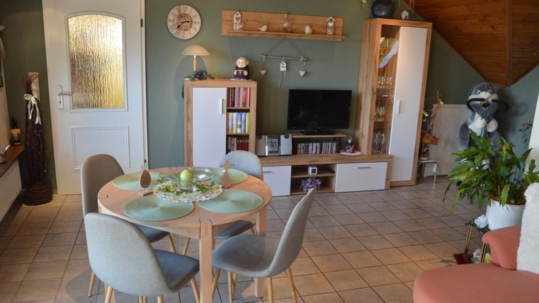A cozy living space with a round table and modern chairs. On the walls, there are bookshelves and a TV corner.