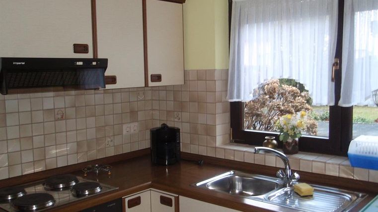 Une cuisine lumineuse avec des surfaces en bois et des carreaux clairs. Il y a des fleurs sur la fenêtre et la lumière entre.