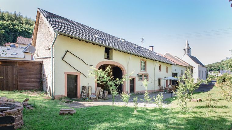Ein altes Bauernhaus mit einem hellen, freundlichen Äußeren. Umgeben von einem schönen Garten und einer ruhigen Landschaft.