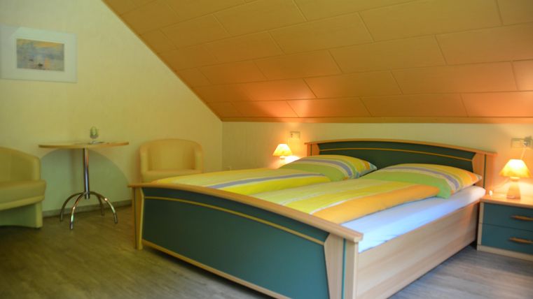 A cozy bedroom with a large double bed and two chairs. The room has a warm atmosphere with soft lighting.