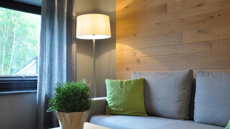 Un espace de vie confortable avec un canapé gris et des coussins verts. Une lampe sur pied et une fenêtre avec des rideaux complètent l'ambiance moderne.