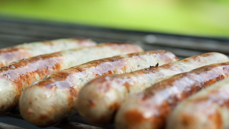 Gegrillte Würstchen liegen auf einem Rost. Sie sind braun und goldbraun gebraten, umgeben von einer unscharfen grünen Hintergrundkulisse.