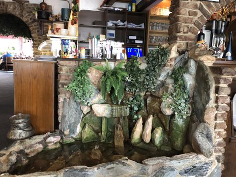 Ein kleiner Wasserfall mit Steinen und Pflanzen in einem Restaurant. Die Umgebung ist gemütlich und einladend.