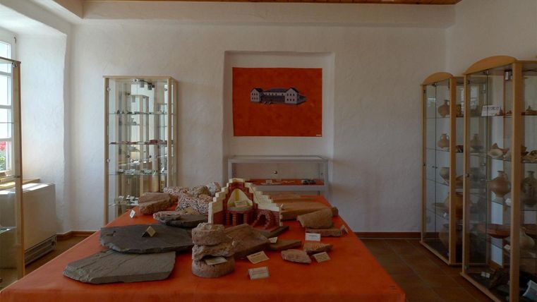 Ein Raum mit Vitrinen, die historische Artefakte ausstellen. Auf dem Tisch sind verschiedene Steine und Objekte angeordnet.