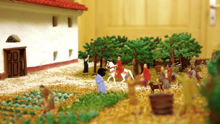 Eine detailreiche Kulisse mit Miniaturfiguren auf einem Bauernhof. Es gibt Bäume, ein Haus und Menschen, die mit Tieren und in der Natur interagieren.