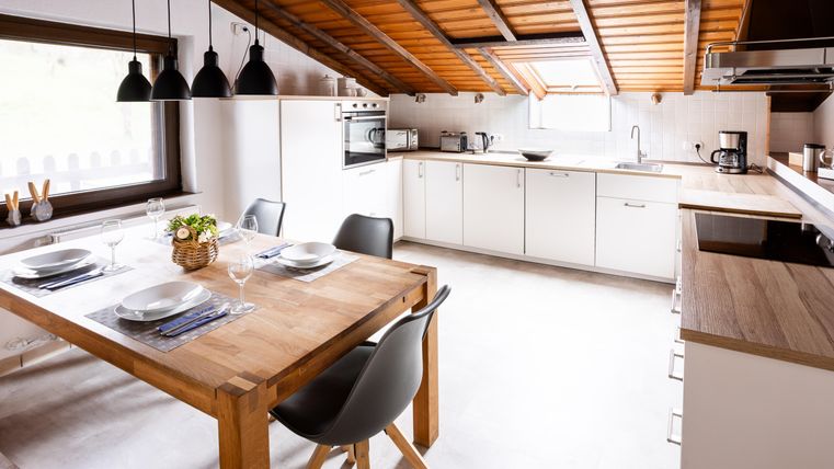 A modern kitchen with a wooden ceiling and light walls. The table is set for a meal and the furnishings are elegant and functional.