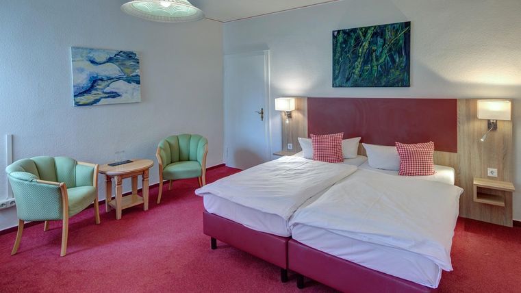 Une chambre d'hôtel confortable avec un lit double et une petite table. Les murs sont clairs, et il y a deux fauteuils confortables.