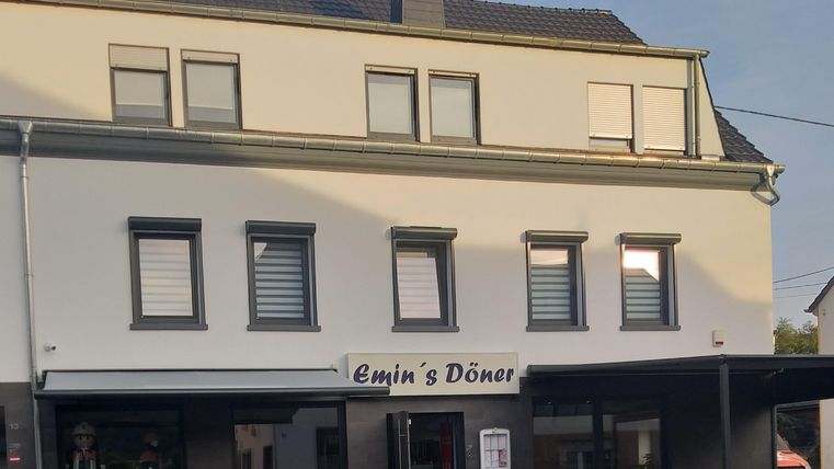 Ein Restaurant namens "Emin's Döner" in einem modernen Gebäude. Die Fassade ist hell, mit Fenstern und einem überdachten Außenbereich.