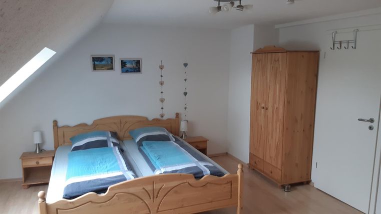 Een gezellige slaapkamer met een houten bed en blauwe dekbedden. Er is een kast en enkele afbeeldingen aan de muur.