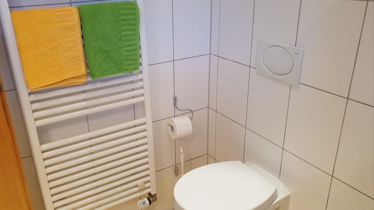 Une salle de bain propre avec des toilettes et des serviettes de différentes couleurs. Un radiateur à serviettes est visible sur le mur.