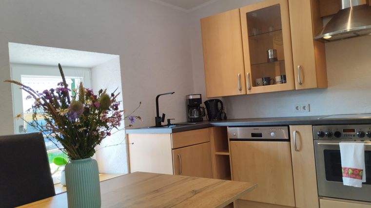 Een moderne keuken met houten meubels en een mooie vaas met bloemen op de tafel. Op de achtergrond zijn er ramen die natuurlijk licht binnenlaten.