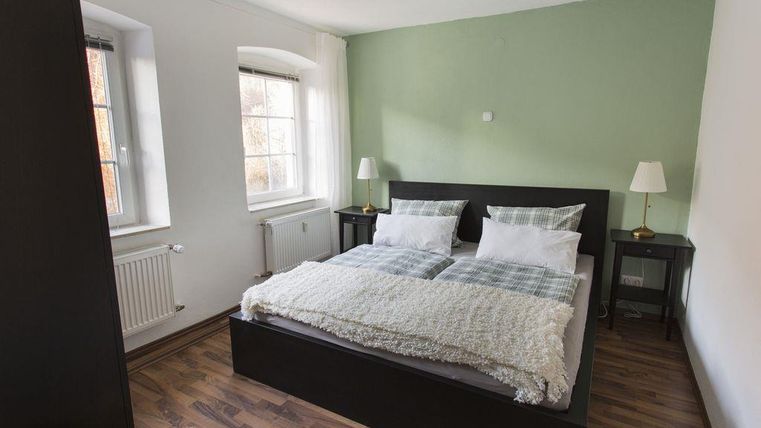 A modern bedroom with a double bed and two nightstands. The walls are painted in a soft color scheme, and there are large windows that let in plenty of light.