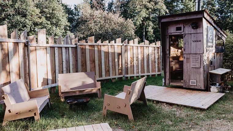 Ein gemütlicher Außenbereich mit einem Holzhaus und bequemen Stühlen. Die grüne Wiese und der Zaun bieten eine ruhige Atmosphäre.