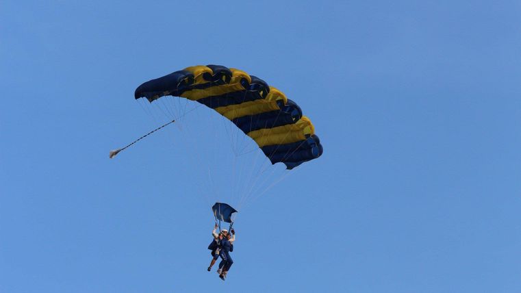 Ein Paraglider schwebt mit einem Passagier durch einen klaren blauen Himmel. Der Fallschirm hat gelbe und blaue Farben.