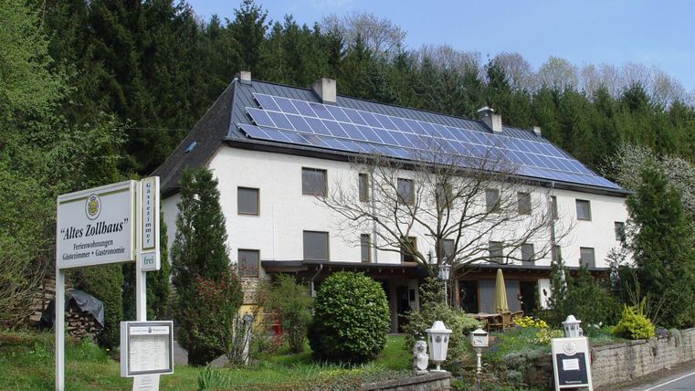 Une maison moderne avec des panneaux solaires sur le toit. Entourée d'arbres et d'un jardin soigné.