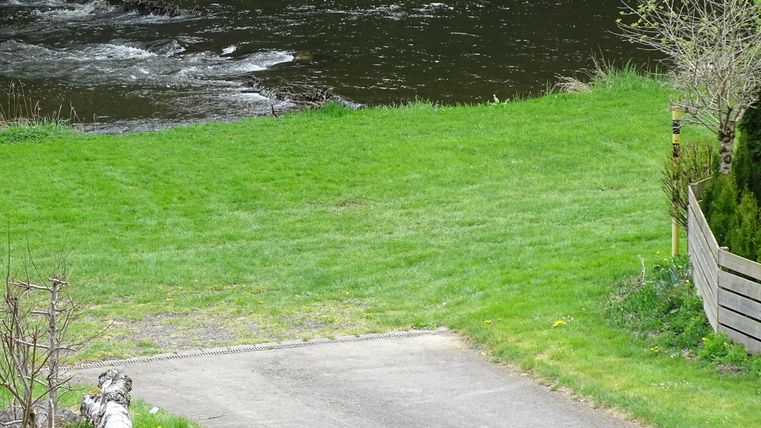 Une rivière calme coule à travers un pré verdoyant. Sur la rive, il y a quelques arbres et un sentier étroit.