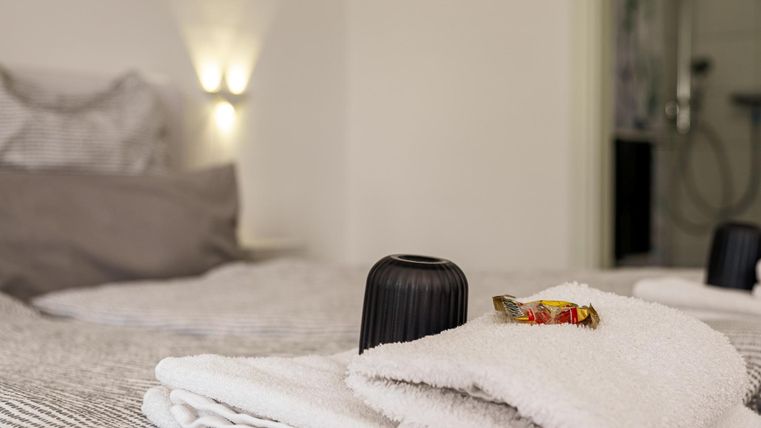 Ein gemütliches Zimmer mit frischen Handtüchern und einer kleinen Aufmerksamkeit auf dem Bett. Sanfte Beleuchtung schafft eine entspannte Atmosphäre.