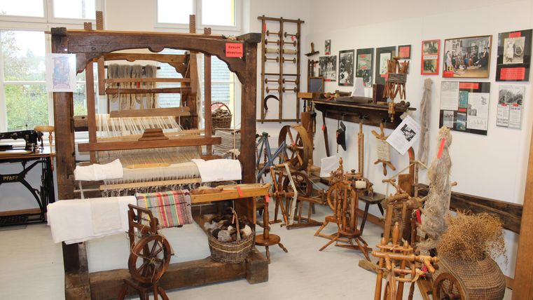 A historical room with various weaving machines and spinning wheels. Photos and information about the history of the craft hang on the walls.