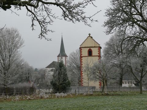 Eine verschneite Landschaft mit zwei Kirchen und frostigen Bäumen. Der Himmel ist grau und bewölkt.