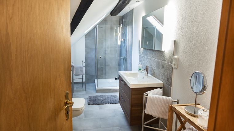 A modern bathroom with a shower and wood details. The room is bright and well-furnished with mirrors and towels.