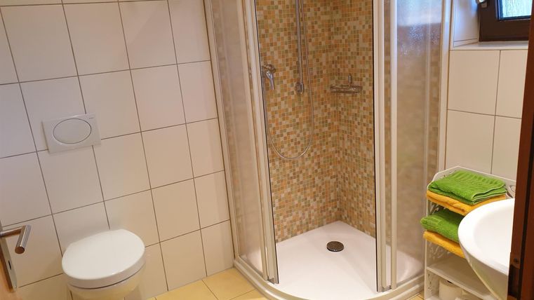 Une salle de bain moderne avec une douche et des toilettes. Il y a des serviettes vertes et un tapis sur le sol.