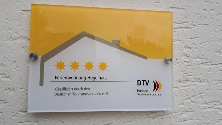Une plaque avec l'inscription « Appartement de vacances Hochhaus » et trois étoiles dorées. La plaque est approuvée par l'Office National Allemand du Tourisme e.V.