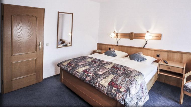 Une chambre confortable avec un grand lit double et des meubles en bois. Les murs sont dans une teinte claire, et un miroir ainsi que des tables de nuit complètent le décor.