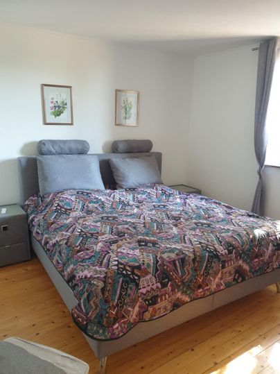 Une chambre confortable avec un grand lit et une literie colorée. Deux tableaux sont accrochés aux murs et une fenêtre assure beaucoup de lumière.