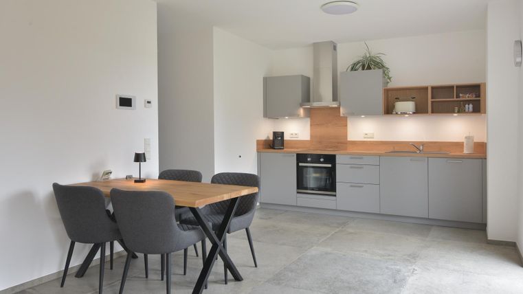 Een moderne keuken met grijze kasten en een houten werkblad. Een eettafel met stoelen staat in het midden van de ruimte.