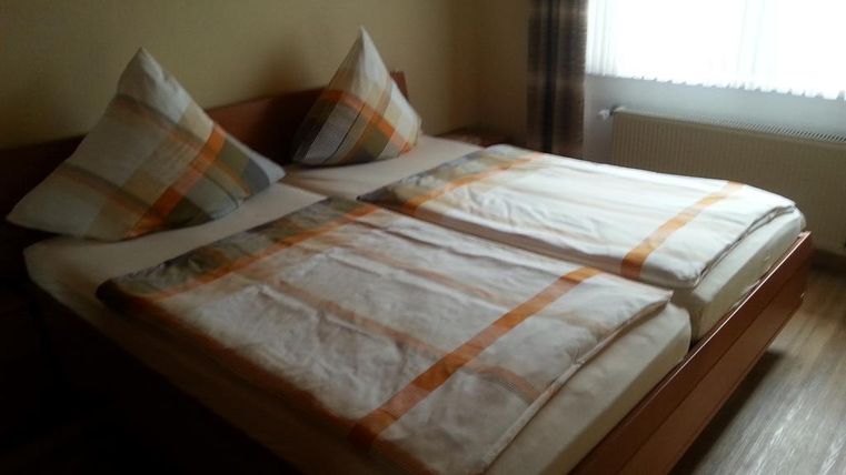 Une chambre simple avec un lit double et deux coussins. La literie est claire et à motifs, et une fenêtre permet à la lumière du jour d'entrer.