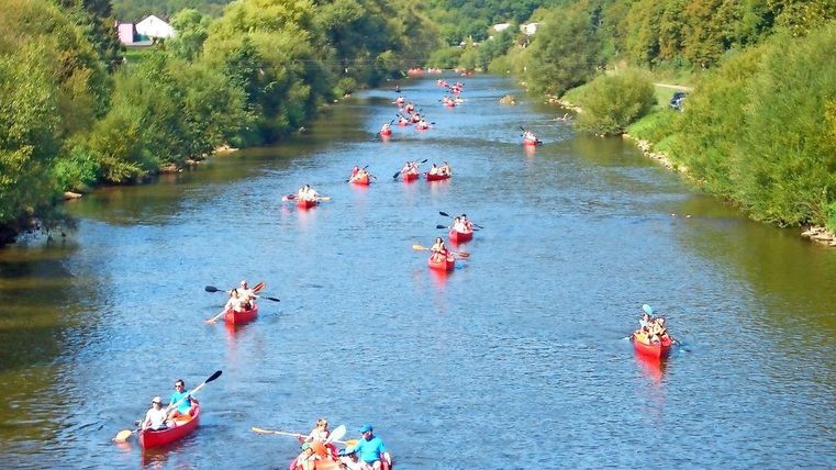 Eine malerische Flusslandschaft mit vielen roten Kanus. Menschen genießen einen aufregenden Tag beim Paddeln in der Natur.