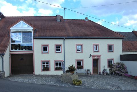 Ein traditionelles, zweigeschossiges Haus mit einem roten Dach und hellen Wänden. Vor dem Haus befinden sich ein kleiner Garten und ein Weg.