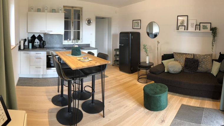 Eine helle und moderne Wohnung mit einer offenen Küche und einem gemütlichen Wohnzimmer. Die Einrichtung ist stylisch und einladend, mit einem Esstisch und einer Eckcouch.