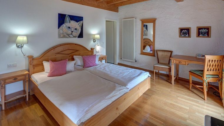 Une chambre confortable avec un lit double et un sol en bois. Les murs sont clairs et décorés d'œuvres d'art, y compris une image d'un chat.