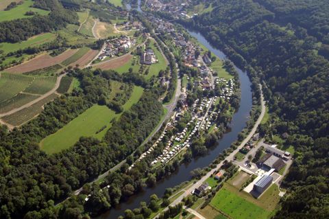 Een luchtfoto van een schilderachtig rivierdale met huizen en weilanden. Omgeven door groene heuvels en bossen stroomt de rivier rustig door het landschap.