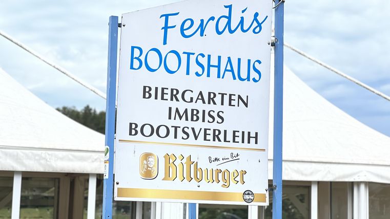 A sign for Ferdi's boathouse, which offers a beer garden, a snack bar, and boat rentals. The surroundings seem inviting and friendly.