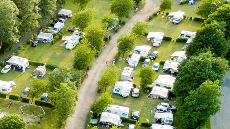 Een camping met veel caravanen en bomen. Er is een helder pad tussen de staanplaatsen.