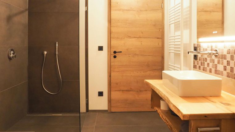 Ein modernes Badezimmer mit einer großzügigen Dusche und einem eleganten Waschbecken. Die Wände sind in dunklen Tönen gehalten, ergänzt durch Holzdetails.