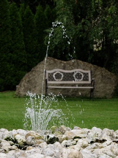 Ein schöner Garten mit einem Springbrunnen aus Wasser und einer Bank im Hintergrund. Die Umgebung ist grün und einladend.