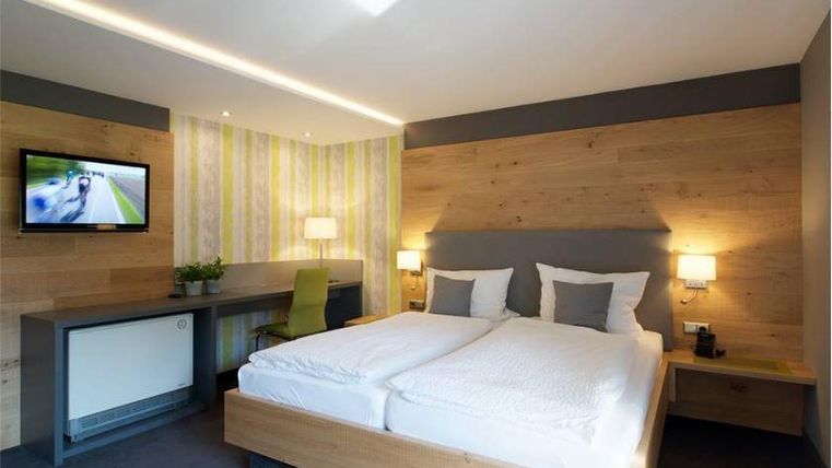 Une chambre d'hôtel moderne avec un lit double et une télévision murale. Les murs sont partiellement en bois, et il y a un bureau avec une chaise.