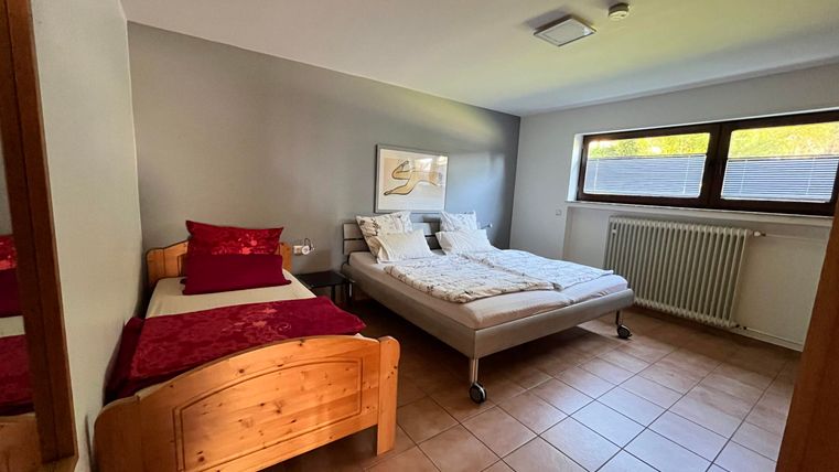 Ein gemütliches Schlafzimmer mit einem Doppelbett und einem Einzelbett. Große Fenster lassen viel Tageslicht hinein.