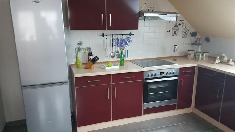 Une cuisine moderne avec des armoires rougeâtre et des carreaux blancs. La pièce est équipée d'un réfrigérateur, d'une cuisinière et d'ustensiles de cuisine.