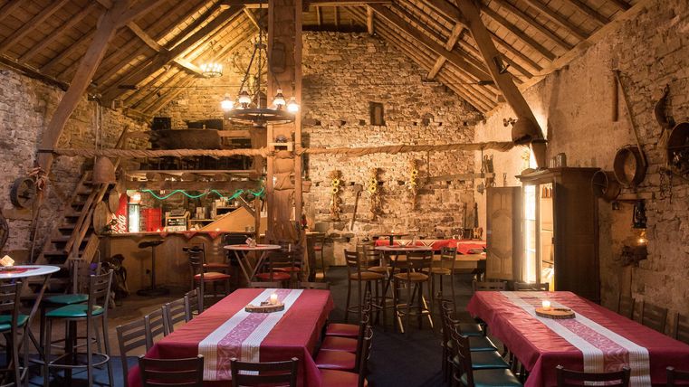 Ein rustikales Restaurant mit Holzbalken und Steinwänden. Tische sind gedeckt und das Ambiente ist gemütlich.