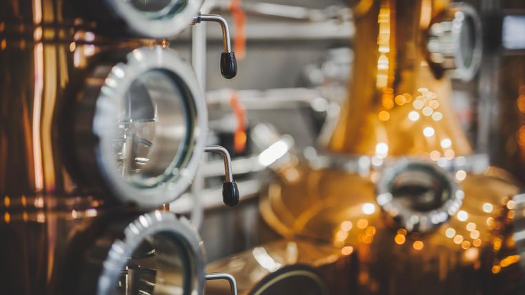 Ein Blick auf eine Kupferdestillerie mit glänzenden Oberflächen und präzisen Steuerungen. Die Details der Maschinen zeigen den Prozess der Alkoholherstellung.
